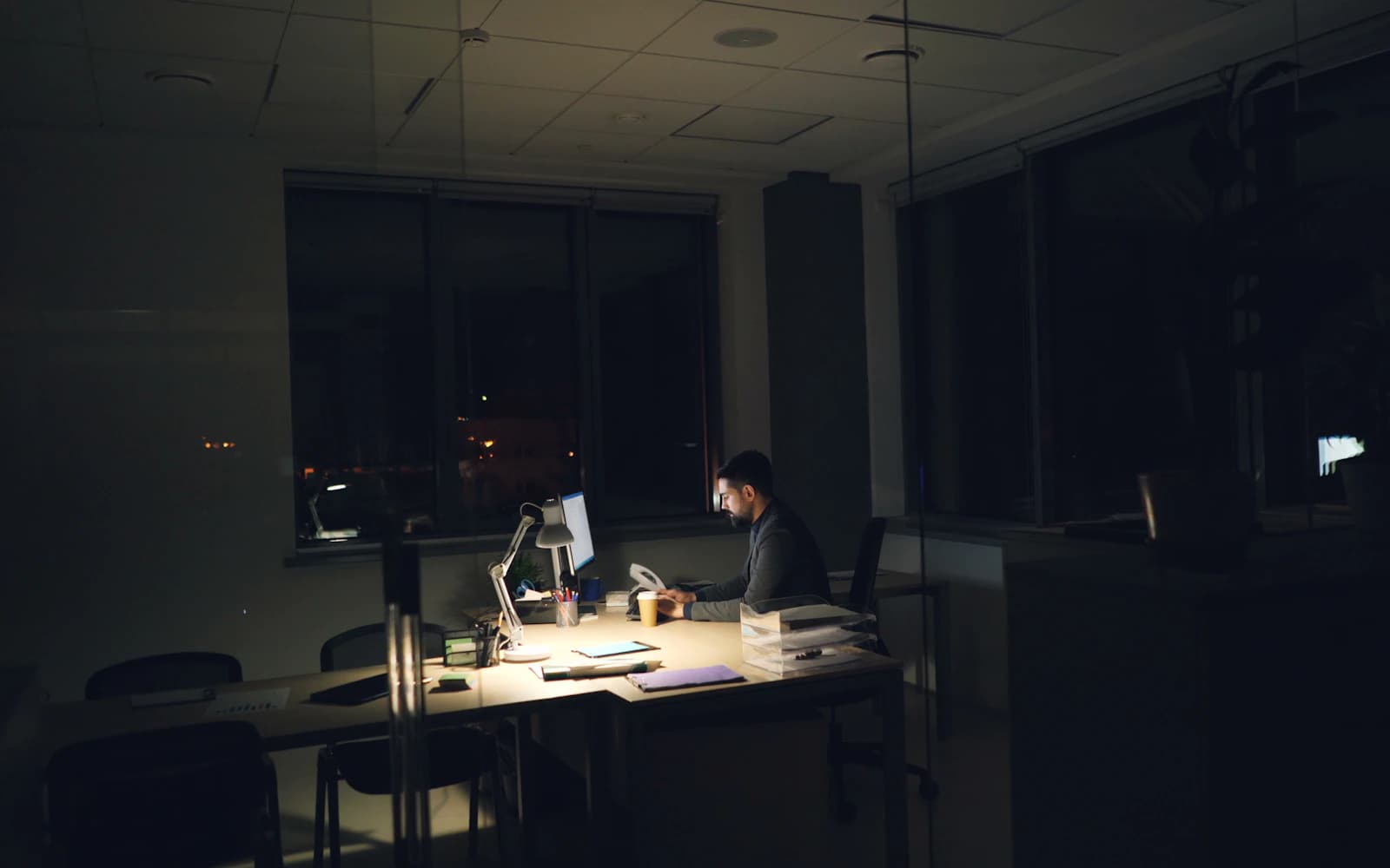 Business owner working late at a lamp-lit desk in an otherwise dark office