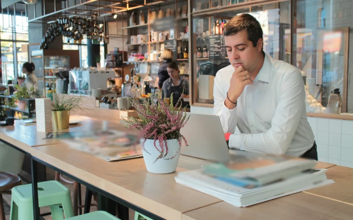 Cafe owner in a white shirt reviewing numbers on a laptop at the long counter of the cafe