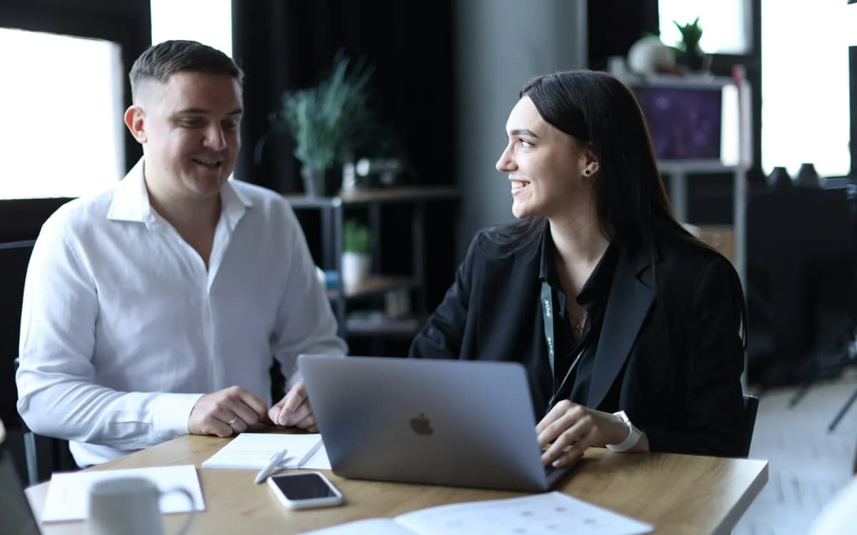 Two people at an office table going over printed notes and a laptop