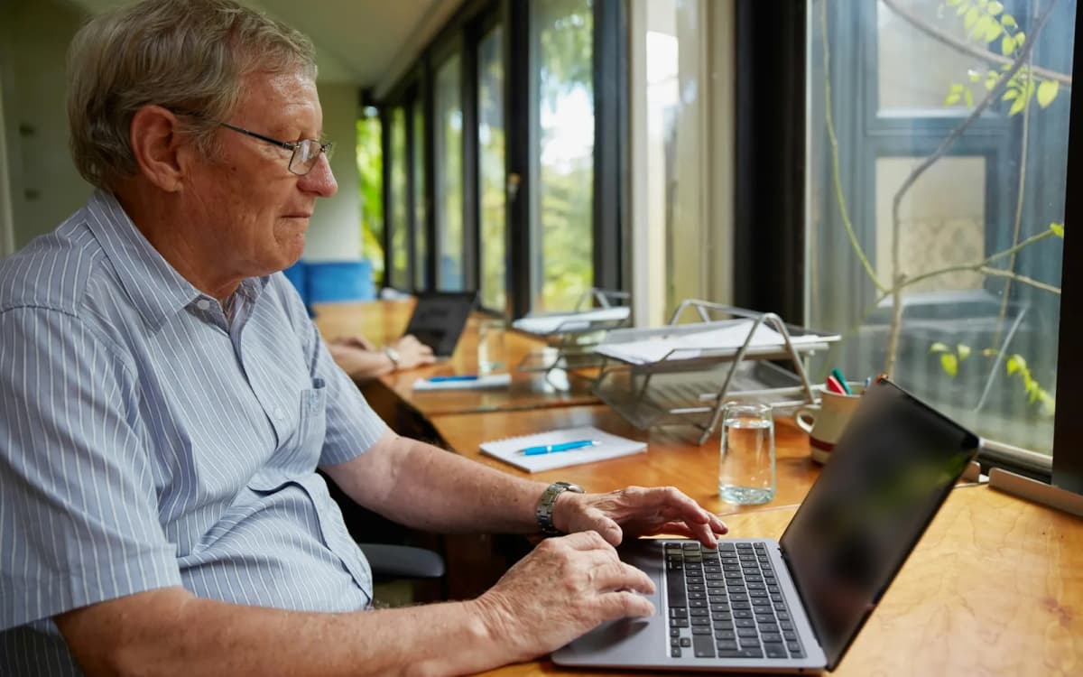 Business owner typing on a laptop at a long desk by a row of sunny windows