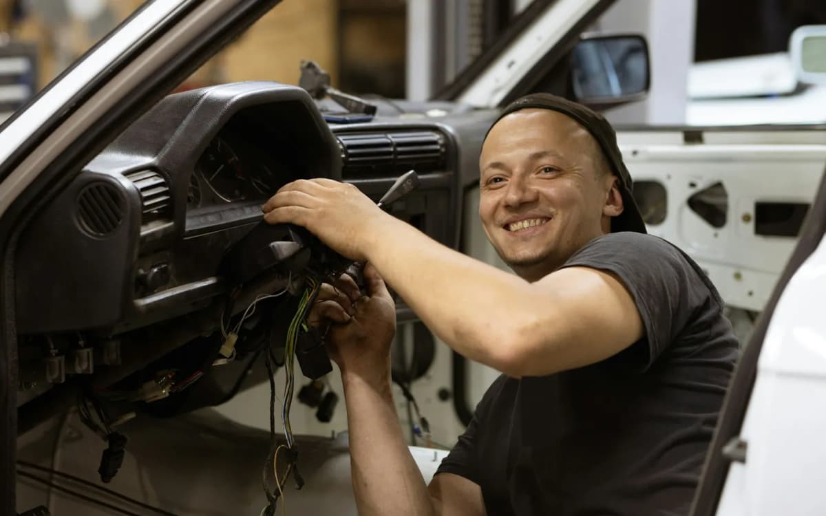 Auto repair shop owner smiling while rewiring a car dashboard in the shop