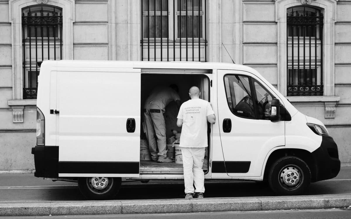 Two workers loading gear through the open side door of a white service van
