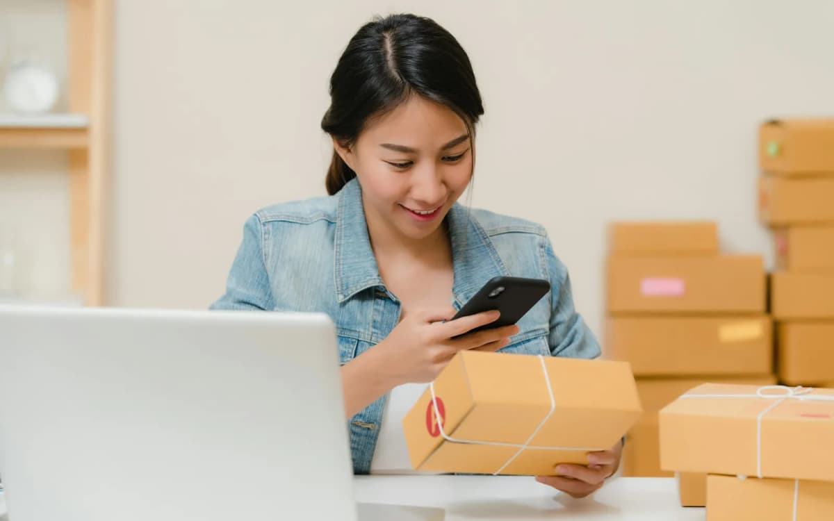 Business owner checking a box of new stock against an order on a phone