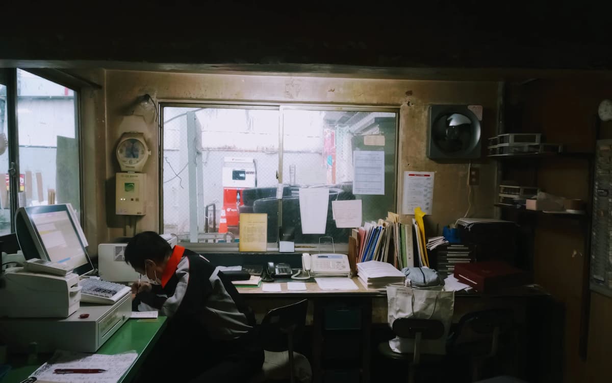 Owner writing figures at a cluttered desk in the back office of a service garage