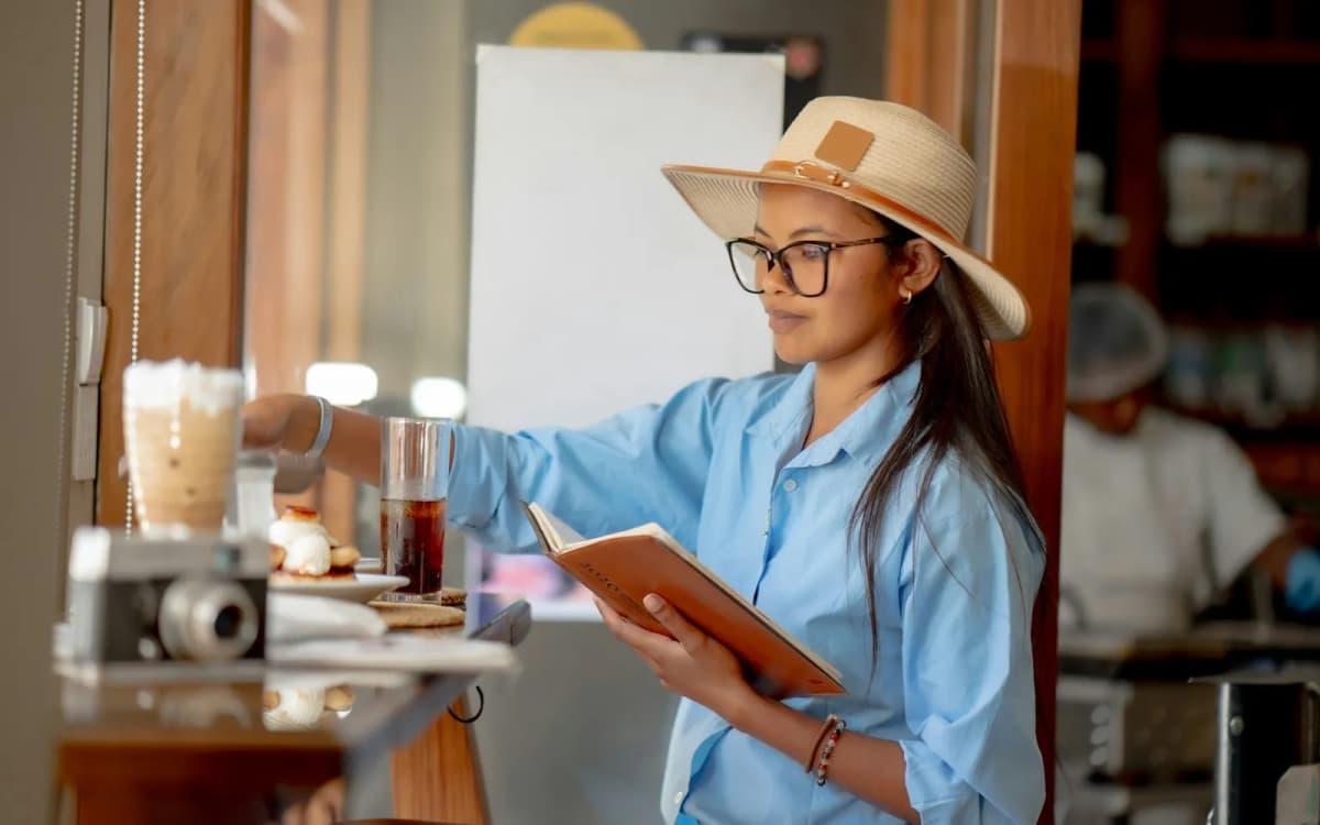 New cafe owner in a straw hat reading a notebook behind the counter