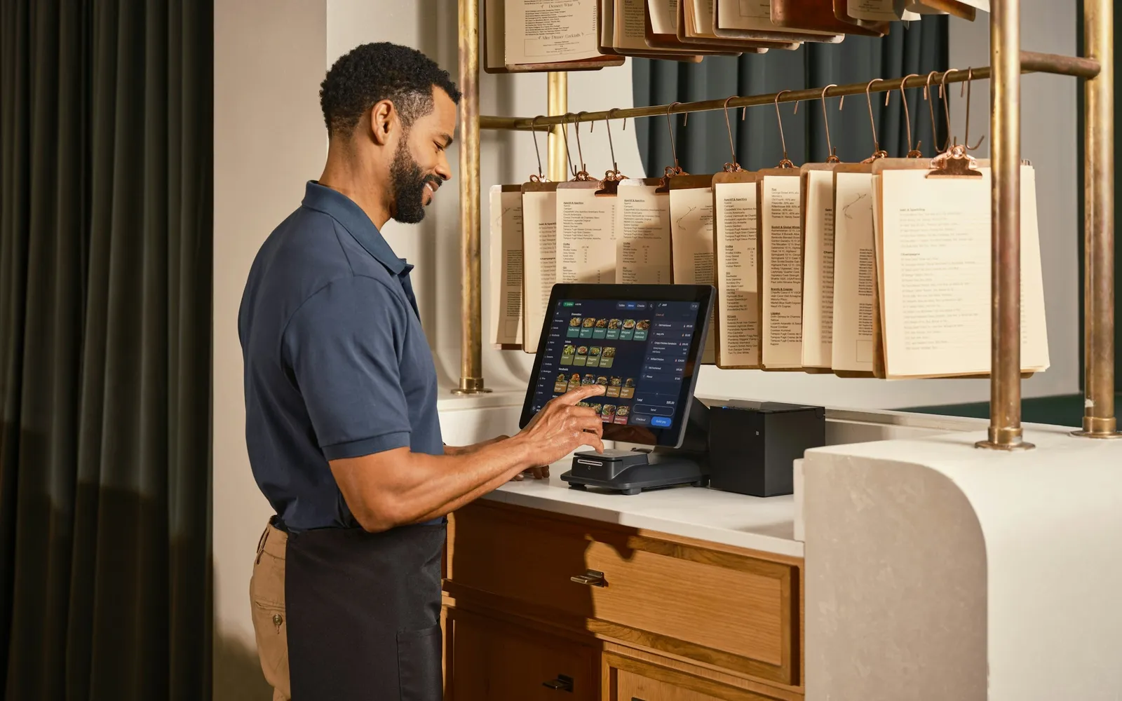 Restaurant owner tapping through the day's orders on a point-of-sale screen behind the counter