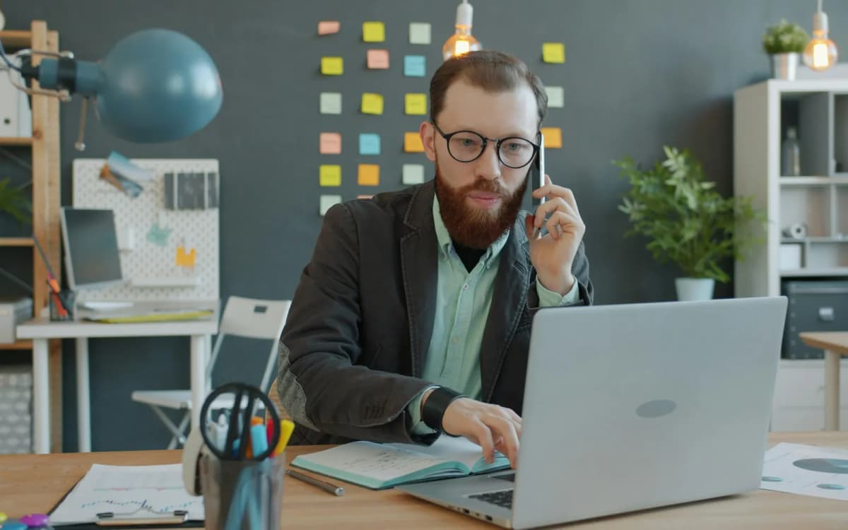 Business owner on the phone at a desk going over funding offers on a laptop