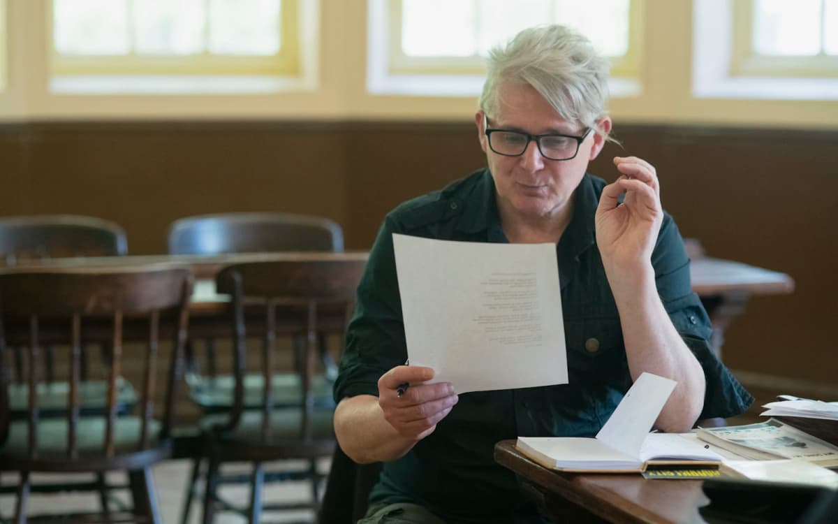 Owner reading a printed page at a wooden table in an empty dining room