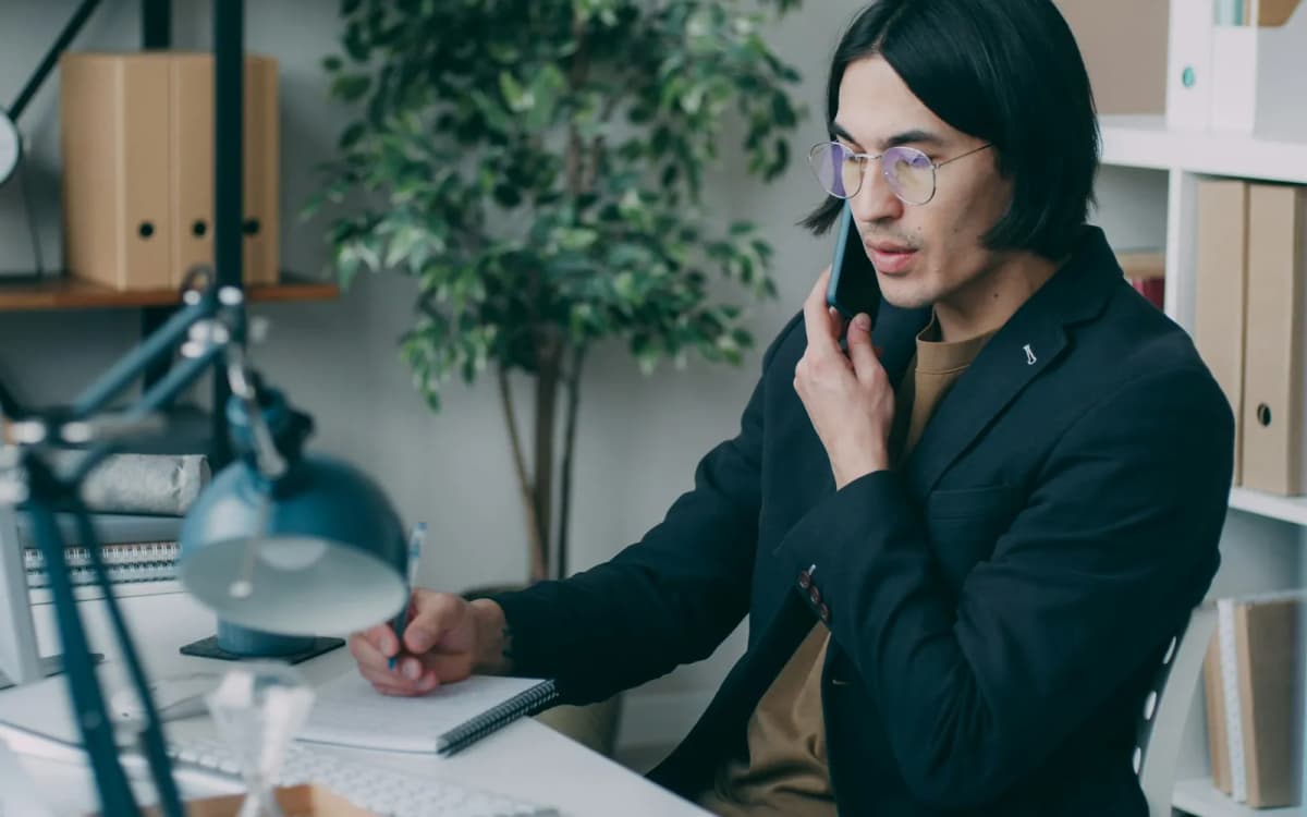 Business owner on a phone call taking notes at a desk beside shelves of folders