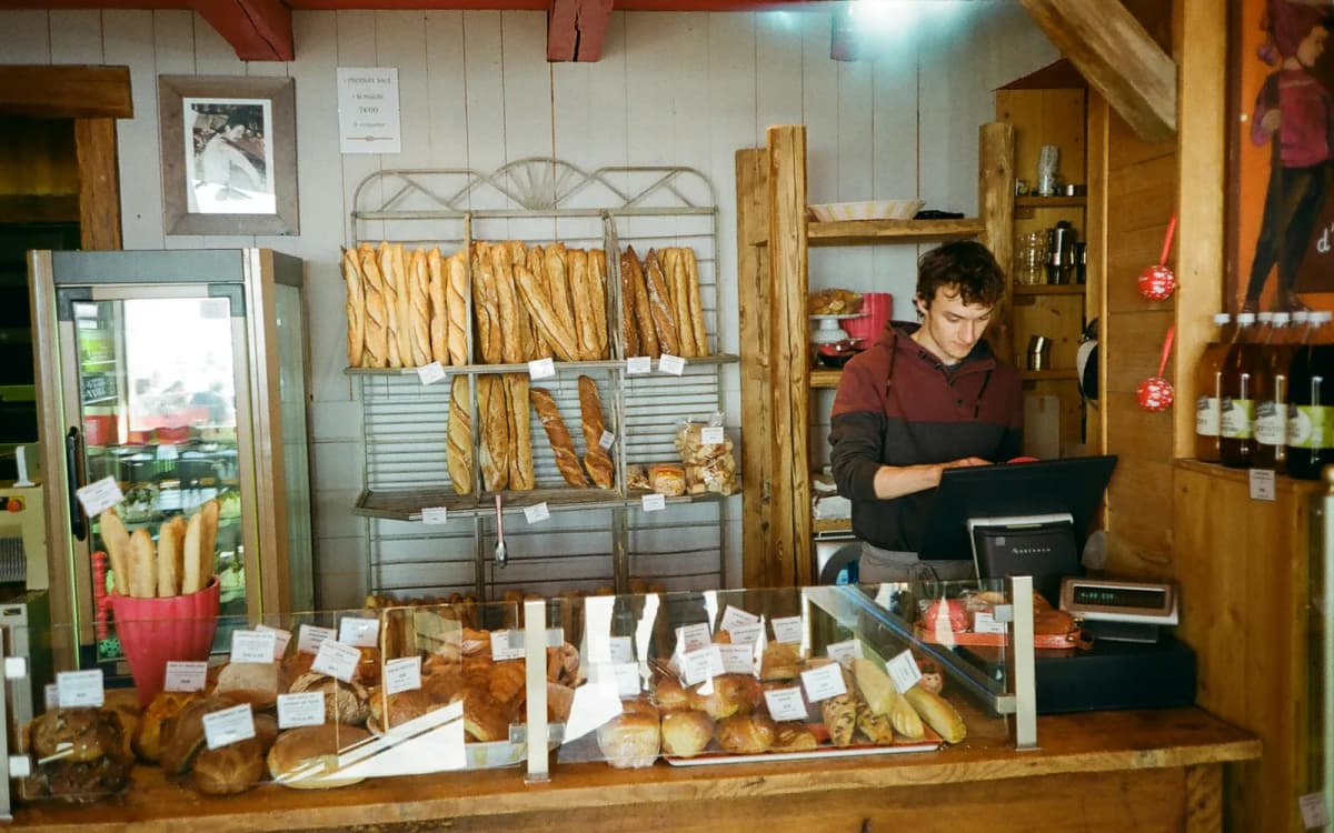 Bakery owner at the counter checking the week's sales on the till screen