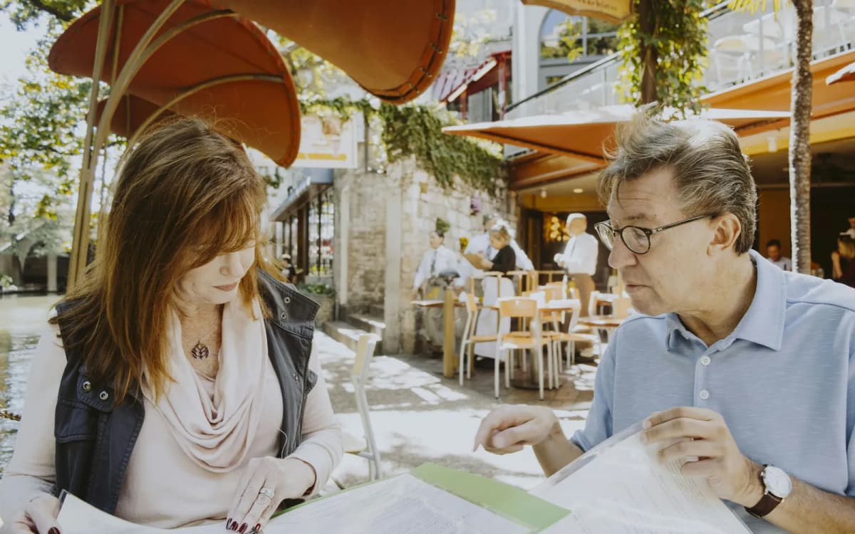 Two people going through the pages of a binder together at an outdoor cafe table