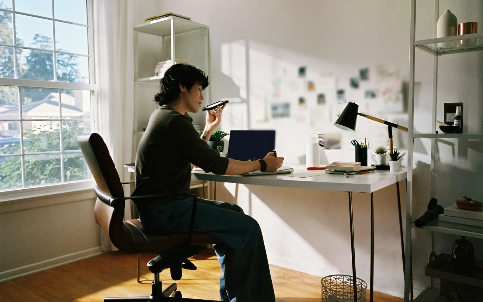 Small business owner on a phone call taking notes at a desk in a sunny home office