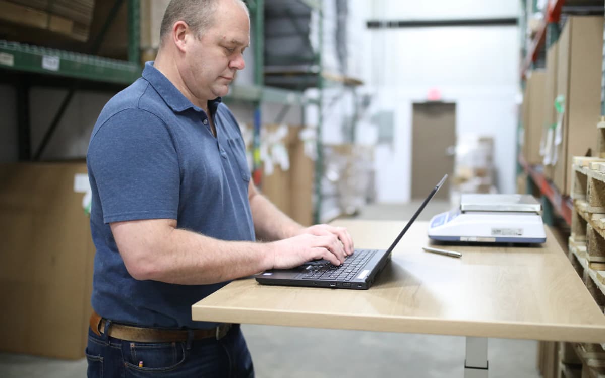 Business owner working on a laptop at a standing desk in his warehouse