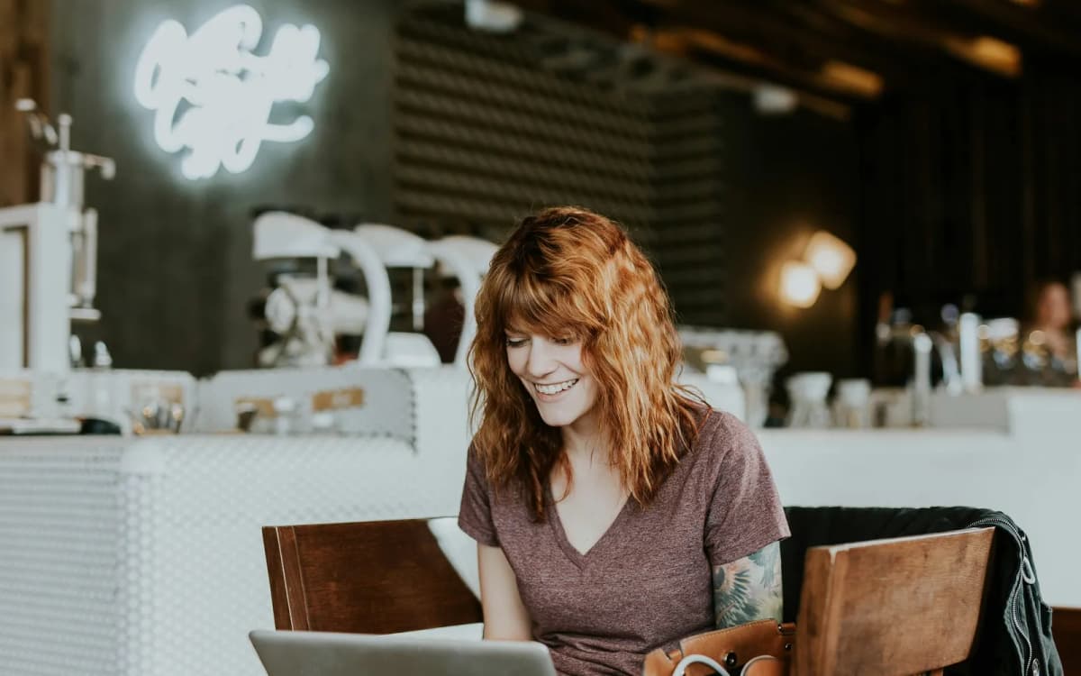 Small business owner smiling at a laptop at a table in a coffee shop