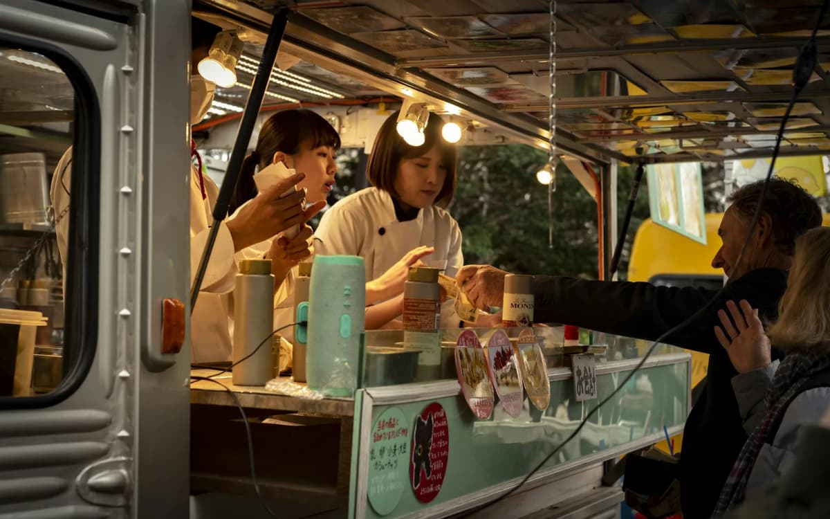 Food truck operators passing an order through the window to a customer at an outdoor market