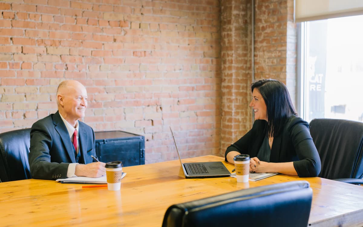 Business owner and an attorney talking across a wooden conference table with notes and a laptop