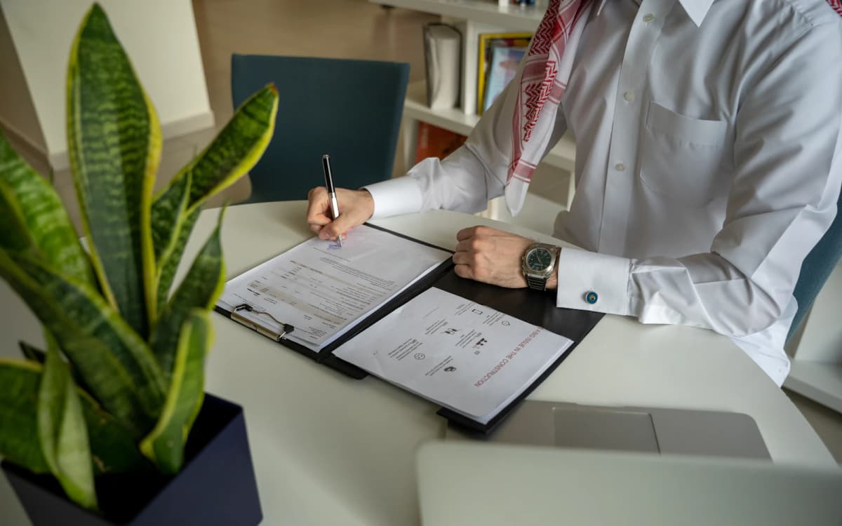 Business owner signing a printed agreement in a folder with a laptop beside it