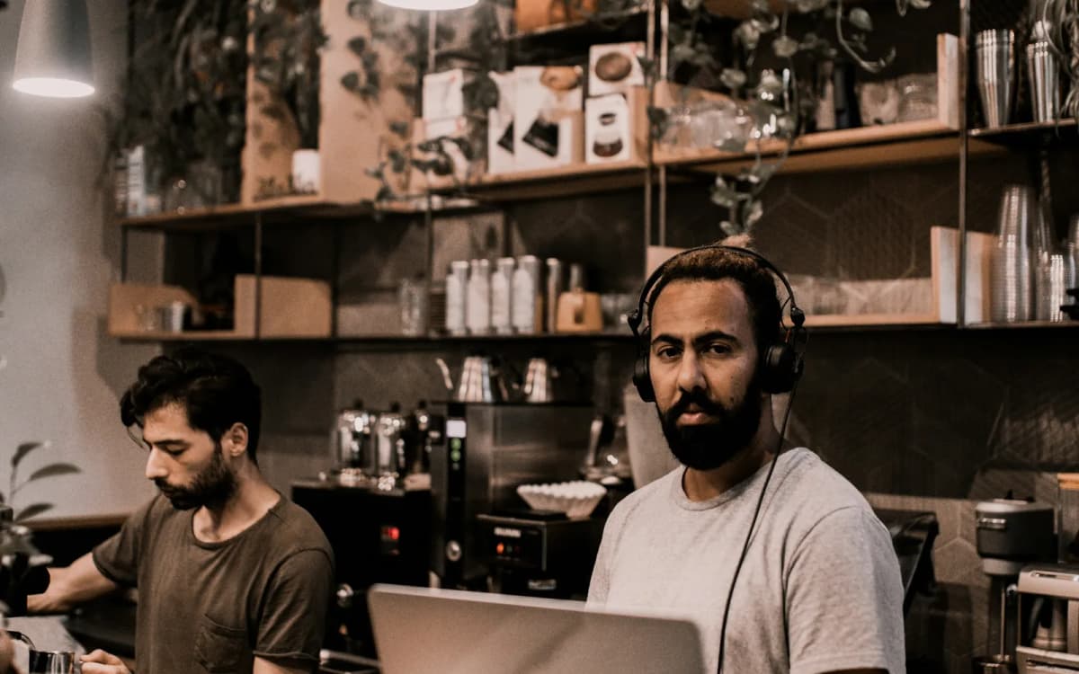 Coffee shop owner at the counter with a laptop while a coworker makes drinks behind