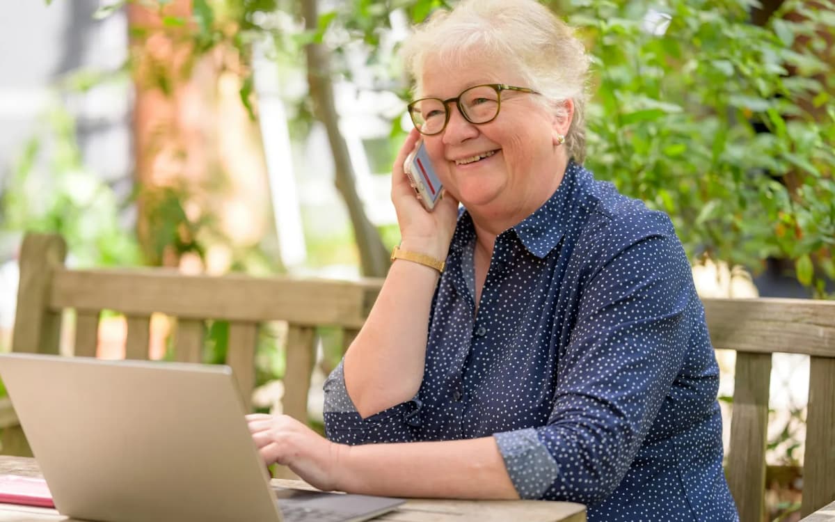 Smiling business owner taking a phone call at a laptop on an outdoor table