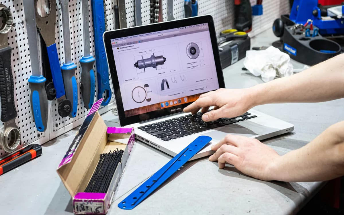 Shop owner working on a laptop at a workbench in front of a tool wall