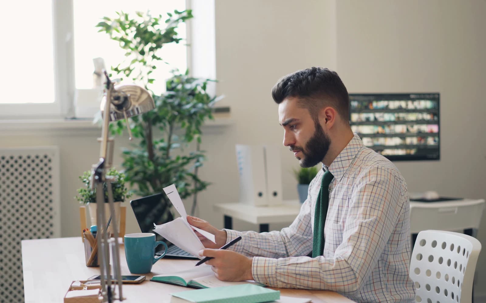 Business owner reading a printed document at his office desk next to a laptop