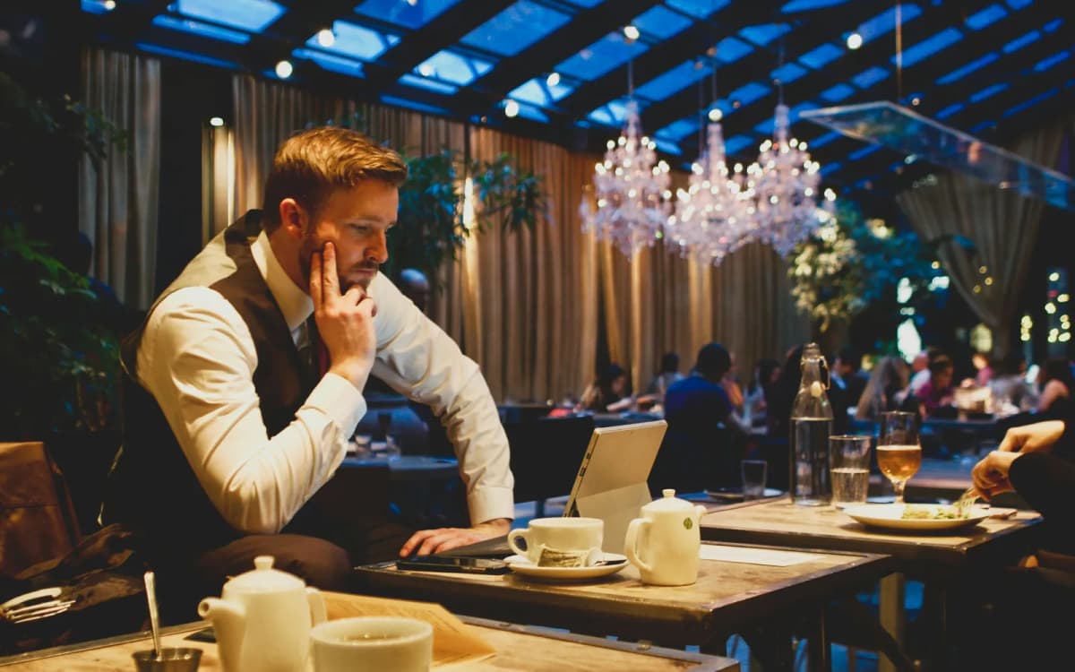 Restaurant owner reviewing business bank statements on a laptop at a dining room table