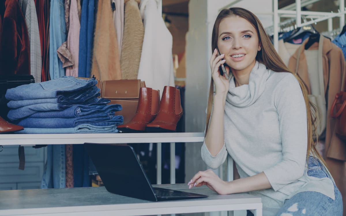 Boutique owner on a phone call at her shop counter with a laptop open