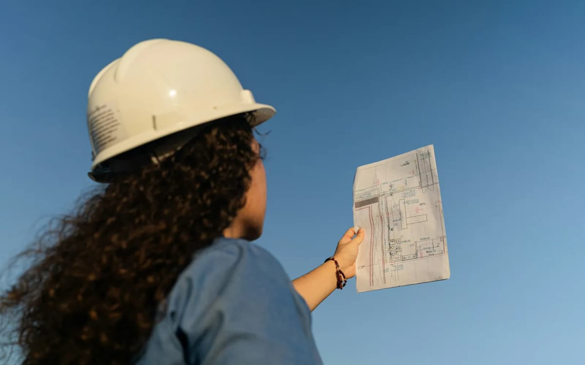 Contractor in a hard hat holding up a printed site plan at a job site