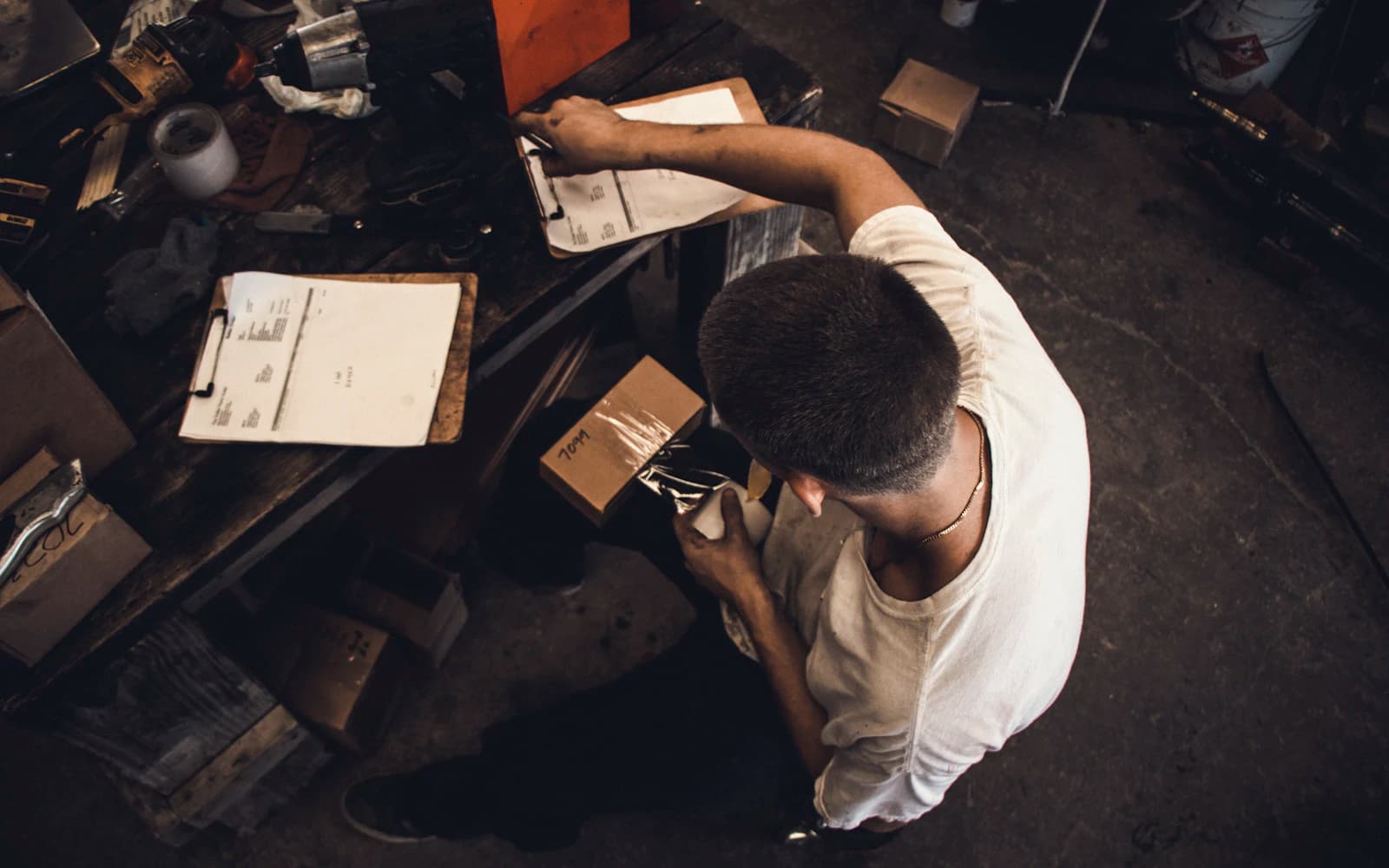 Shop owner checking printed paperwork on clipboards at his workbench