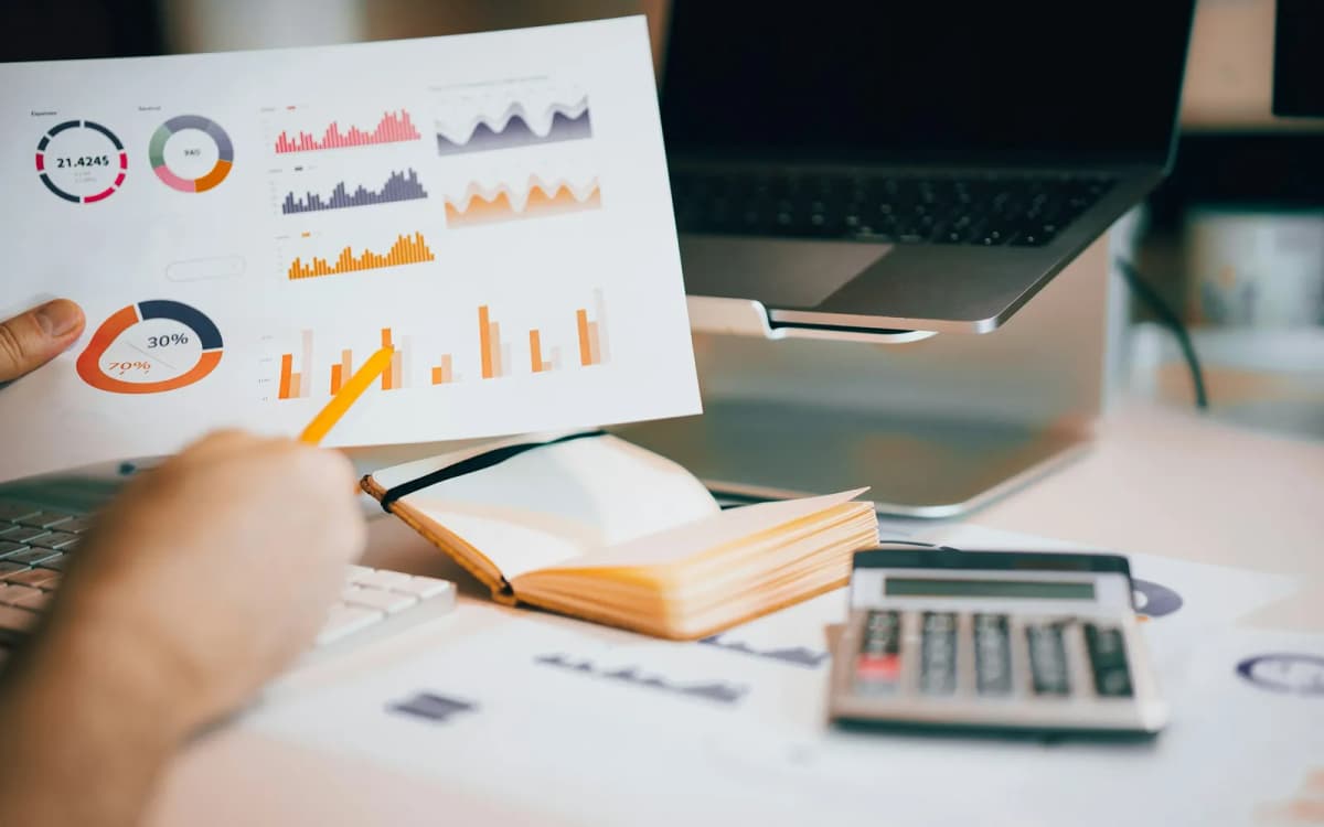 Business owner comparing printed charts with a calculator, notebook and laptop on a desk