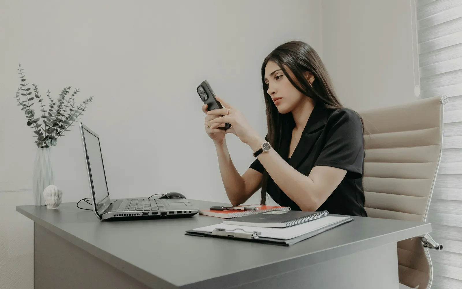 Business owner checking a score on a phone beside an open laptop at a desk
