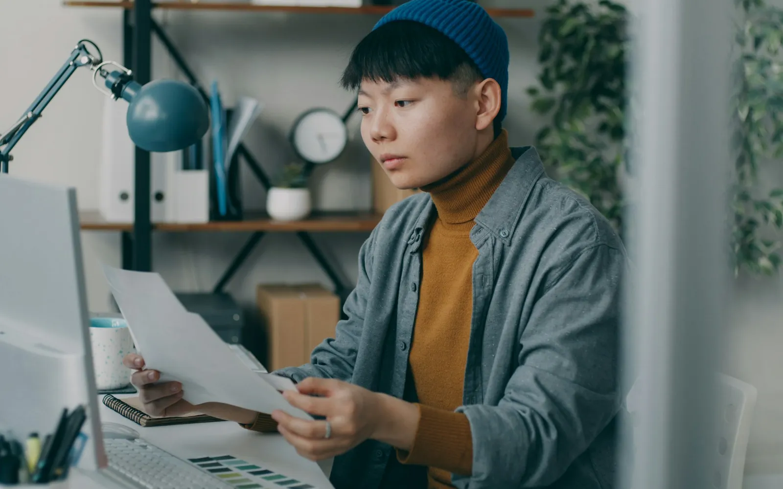 Small business owner reading printed loan paperwork at a desk beside a computer