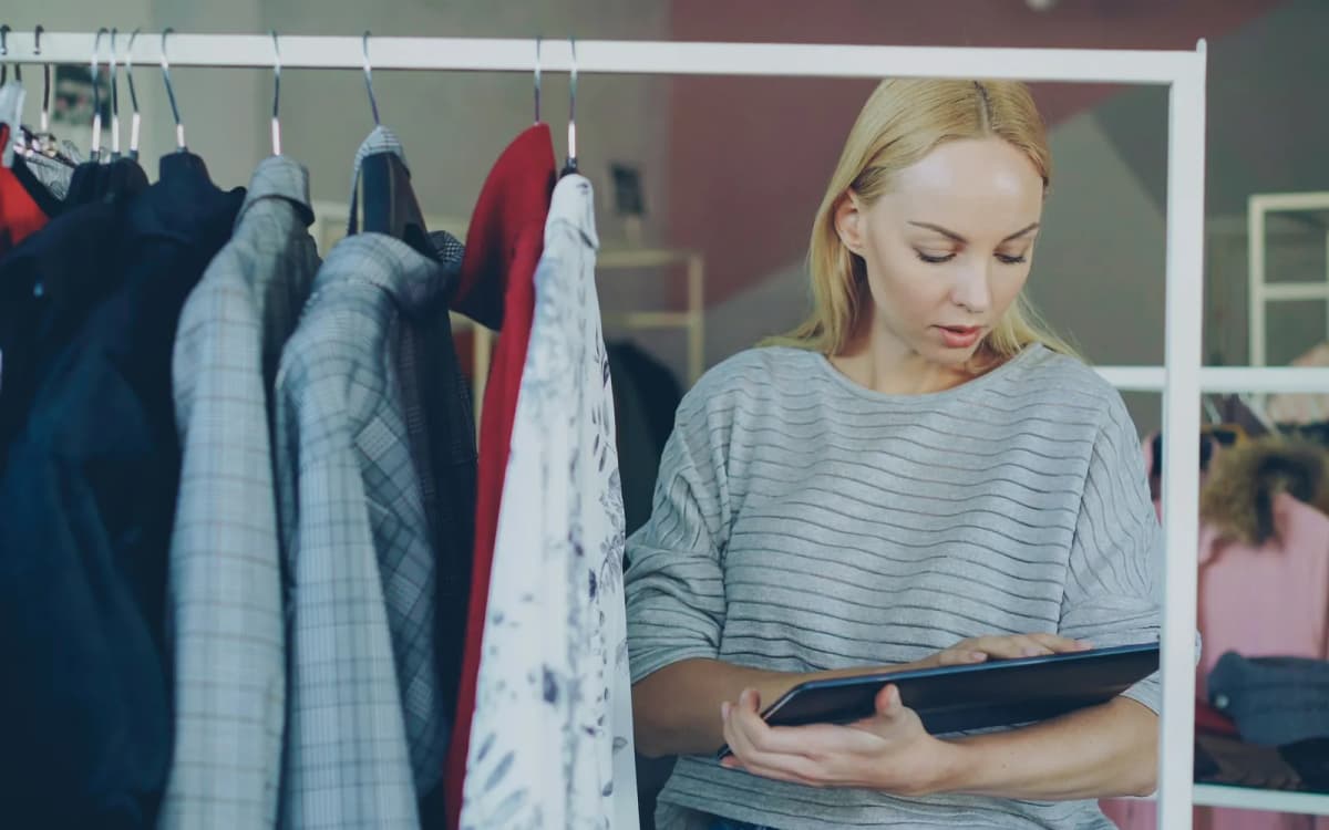 Boutique owner checking stock on a tablet beside a rack of clothes