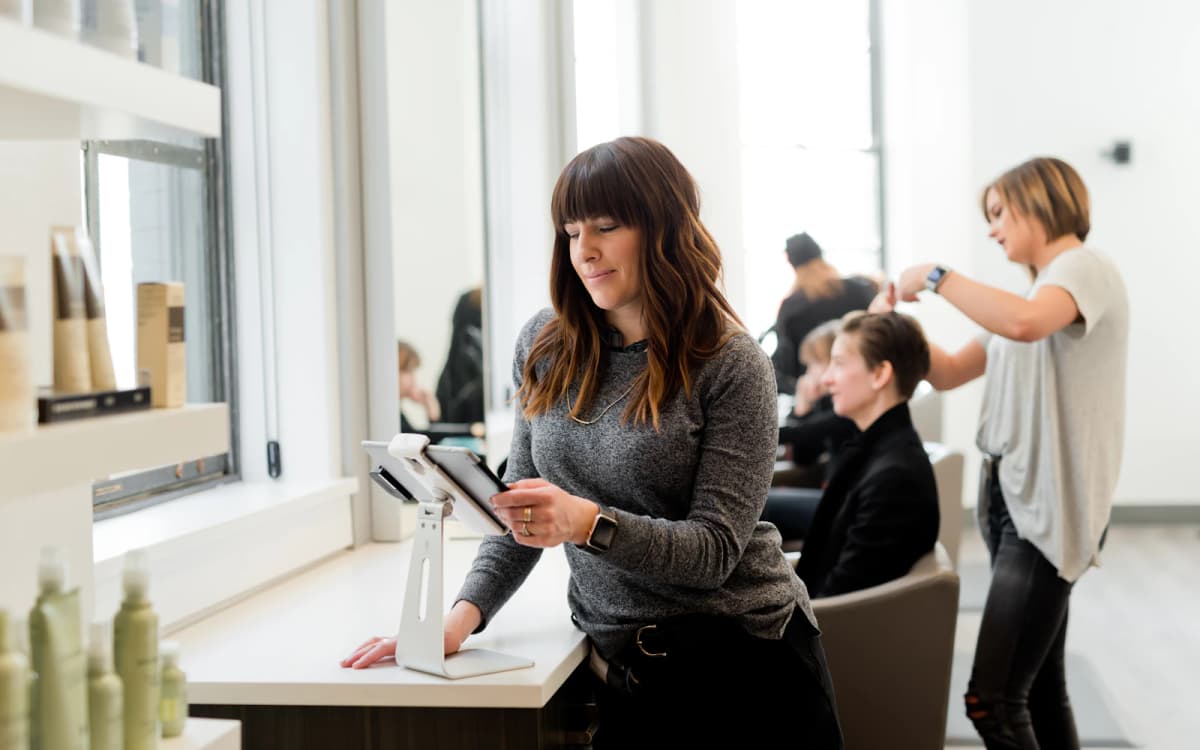 Salon owner reviewing business records on a tablet at the front counter