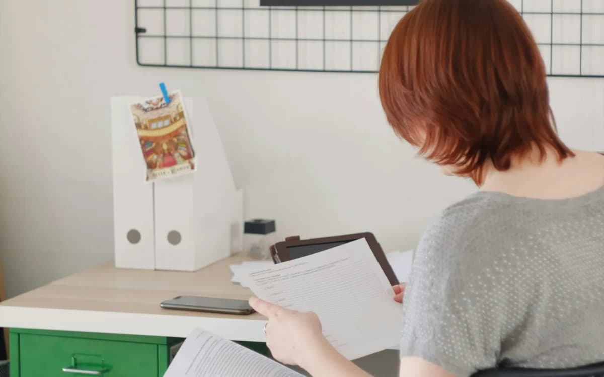 Business owner at a desk reading through printed records with a tablet and phone nearby
