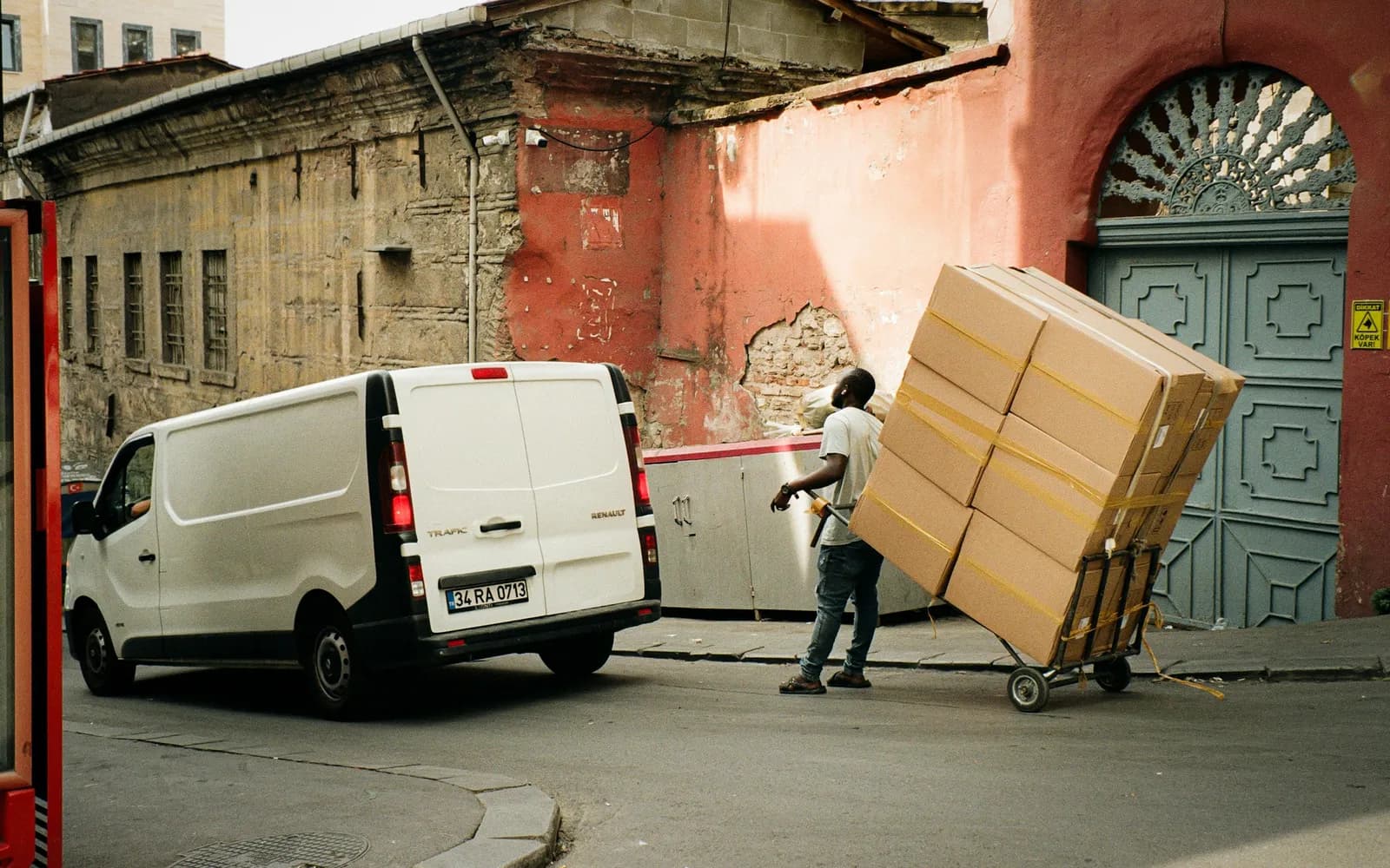 Delivery driver wheeling a tall stack of boxes on a hand truck toward a white van
