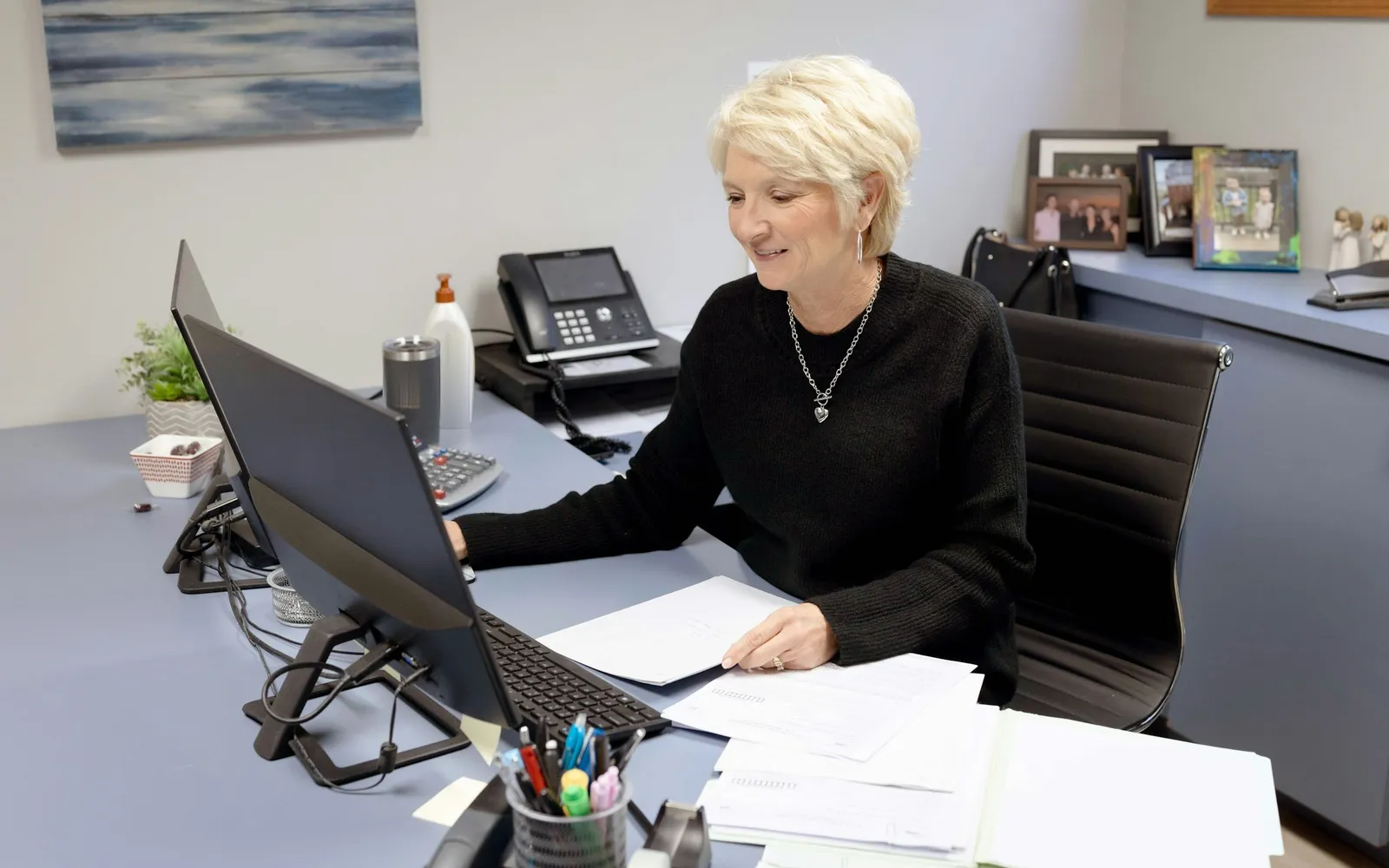 Small business owner going through a stack of statements at an office desk with a computer and calculator