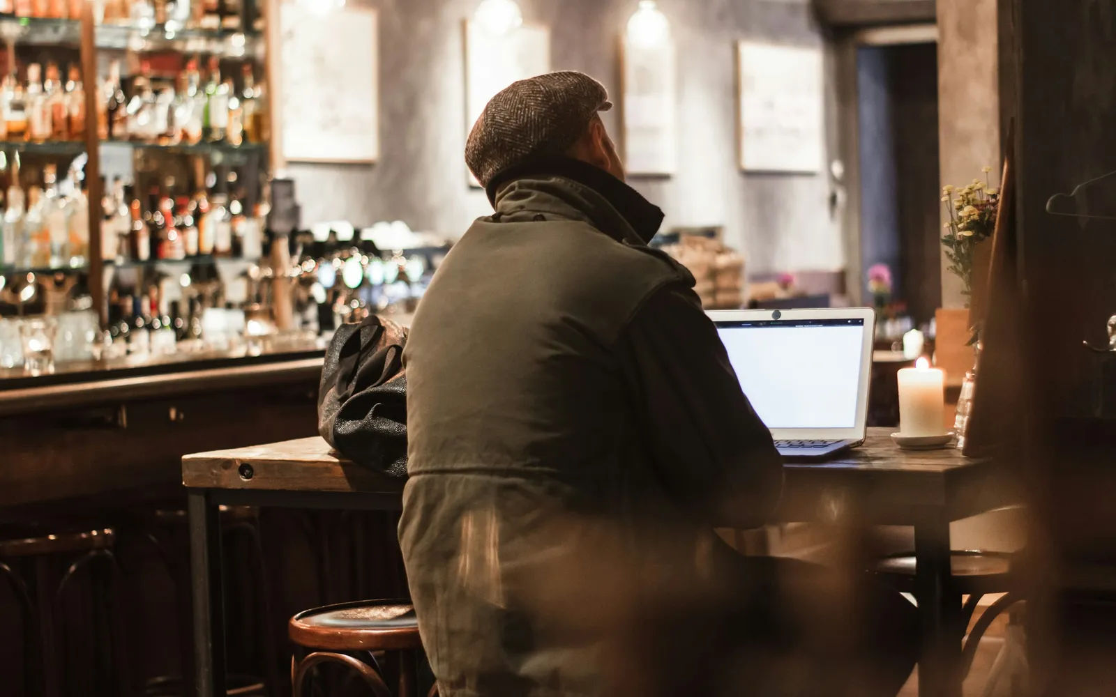 Business owner working on a laptop at a candlelit table in a quiet bar after hours