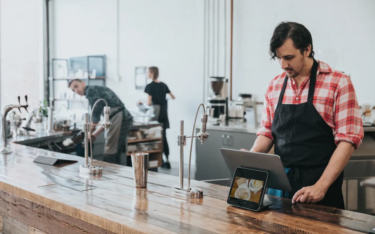 Cafe worker in an apron checking the tablet register at the counter