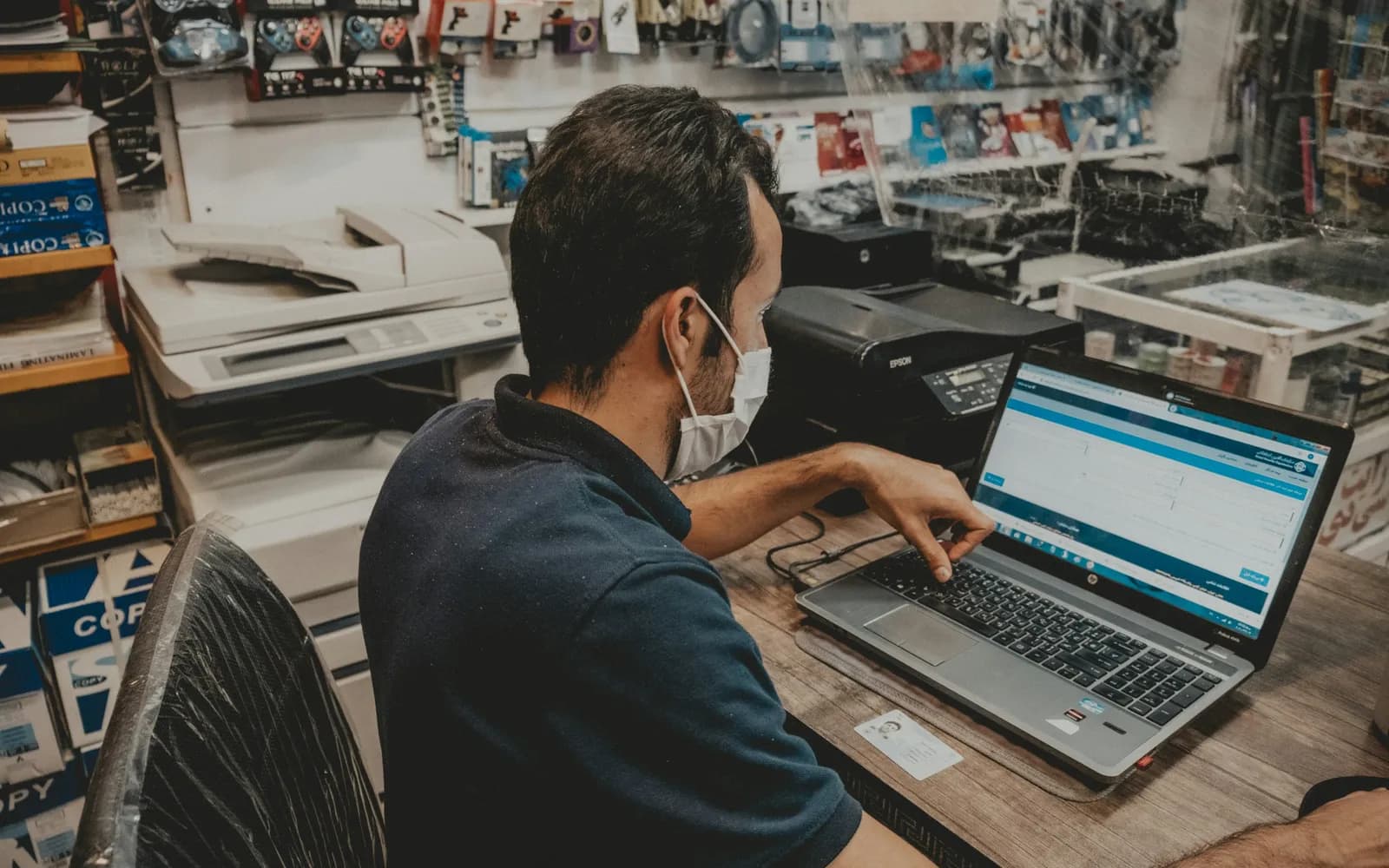 Shop owner comparing figures on a laptop at a desk in a crowded back office