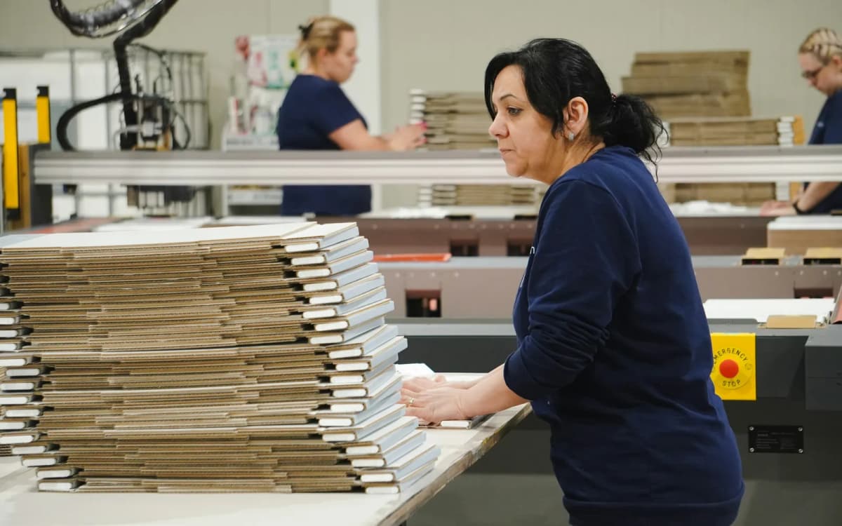 Print shop worker standing beside a cutting machine and stacks of finished products