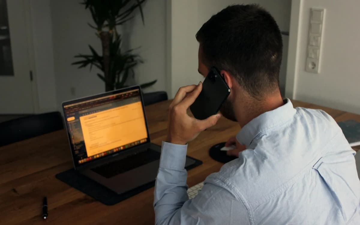 Business owner on a phone call at a wooden desk with a laptop open in front